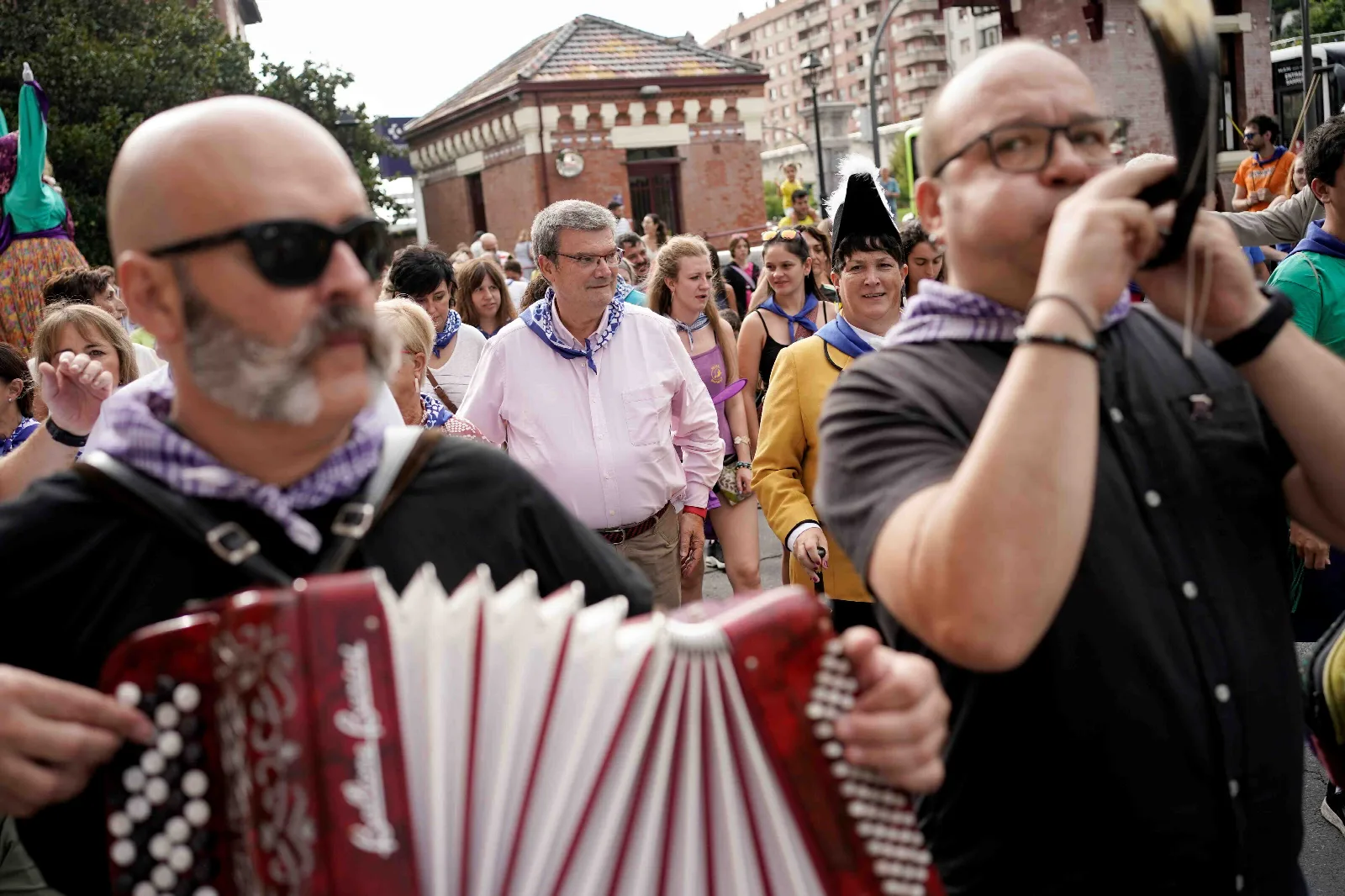 Primer plano de un músico tocando un acordeón rojo y de otro con una pandereta durante el pasacalles