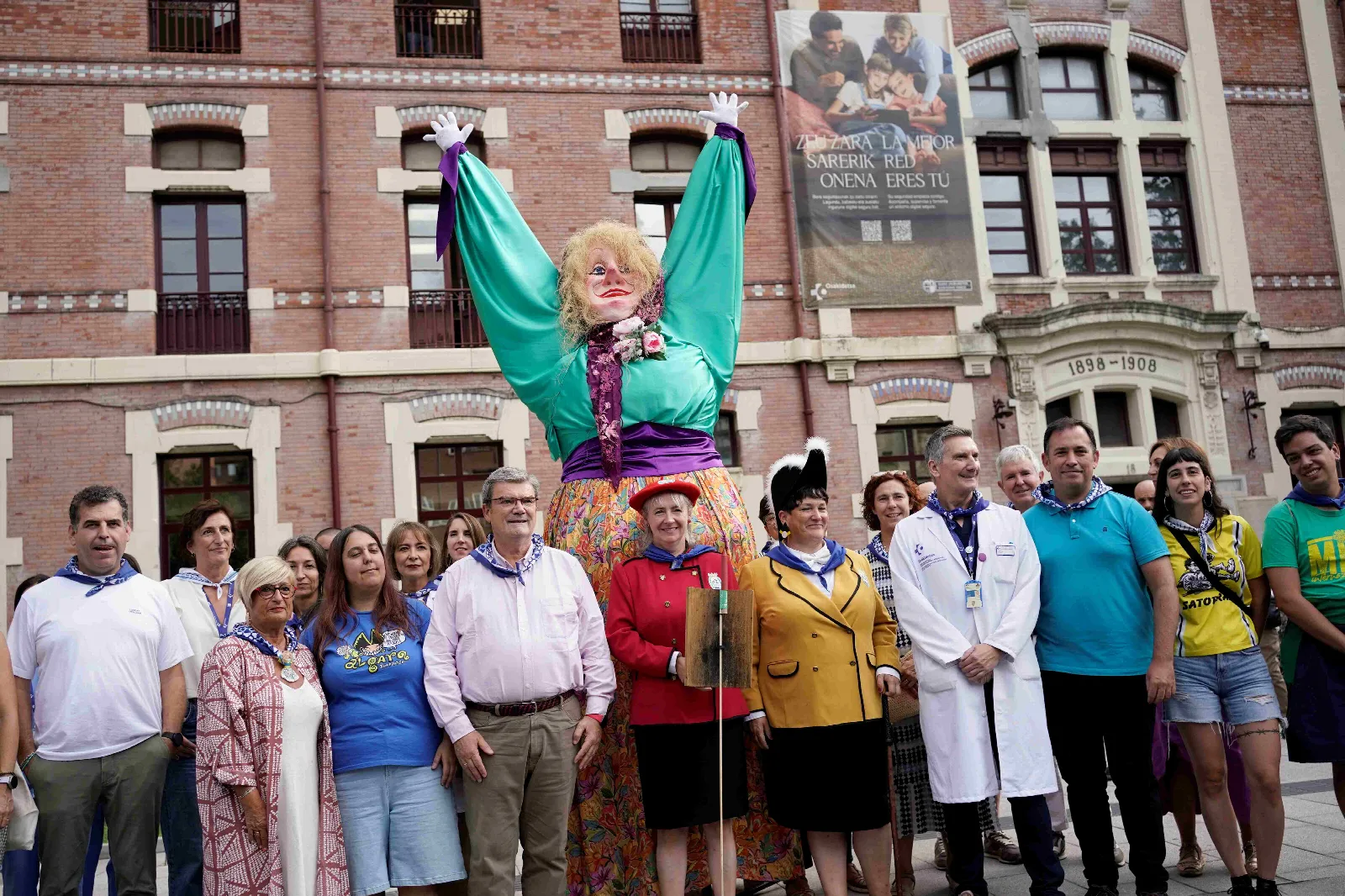 Grupo de representantes municipales y sanitarios posa junto a Marijaia ante la fachada del Pabellón San Pelayo