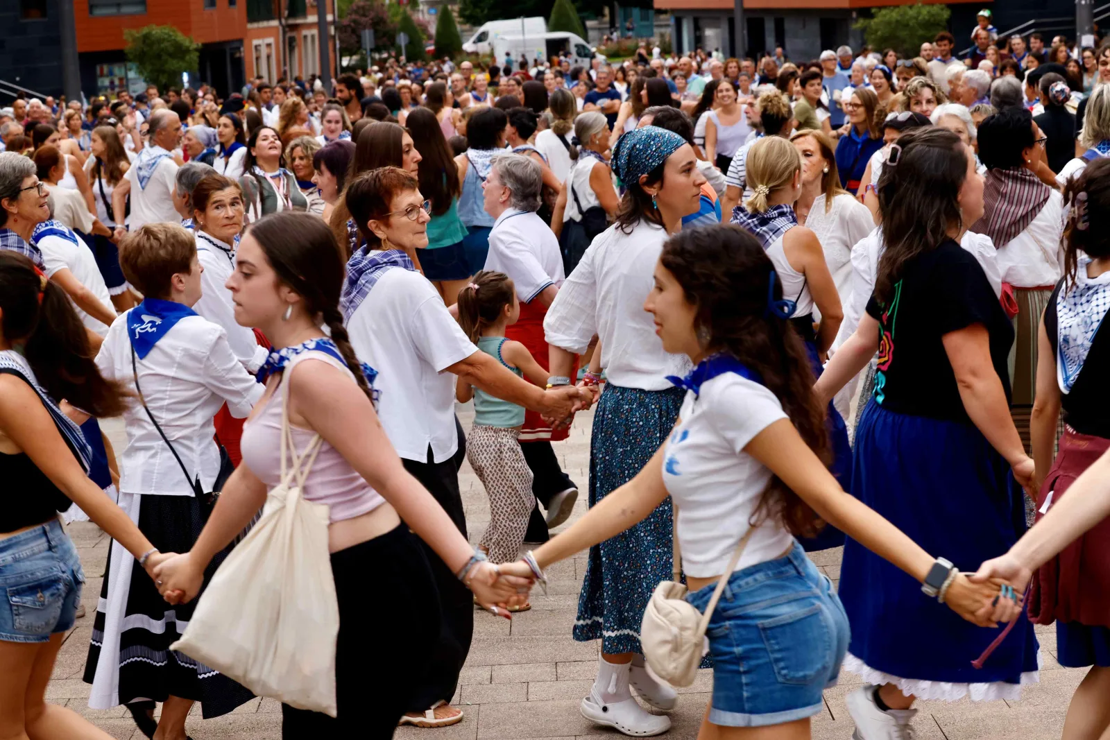 Decenas de personas de todas las edades, en ropa de calle y con pañuelo azul, bailan cogidas de la mano en cadena