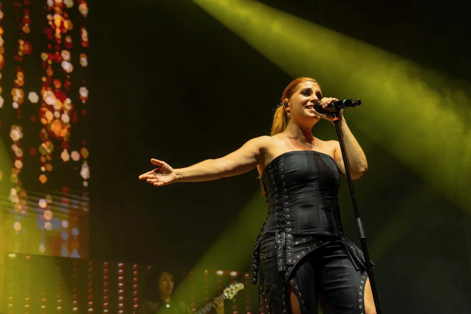 Leire Martínez con el brazo extendido hacia el público, bajo luces verdes y ámbar