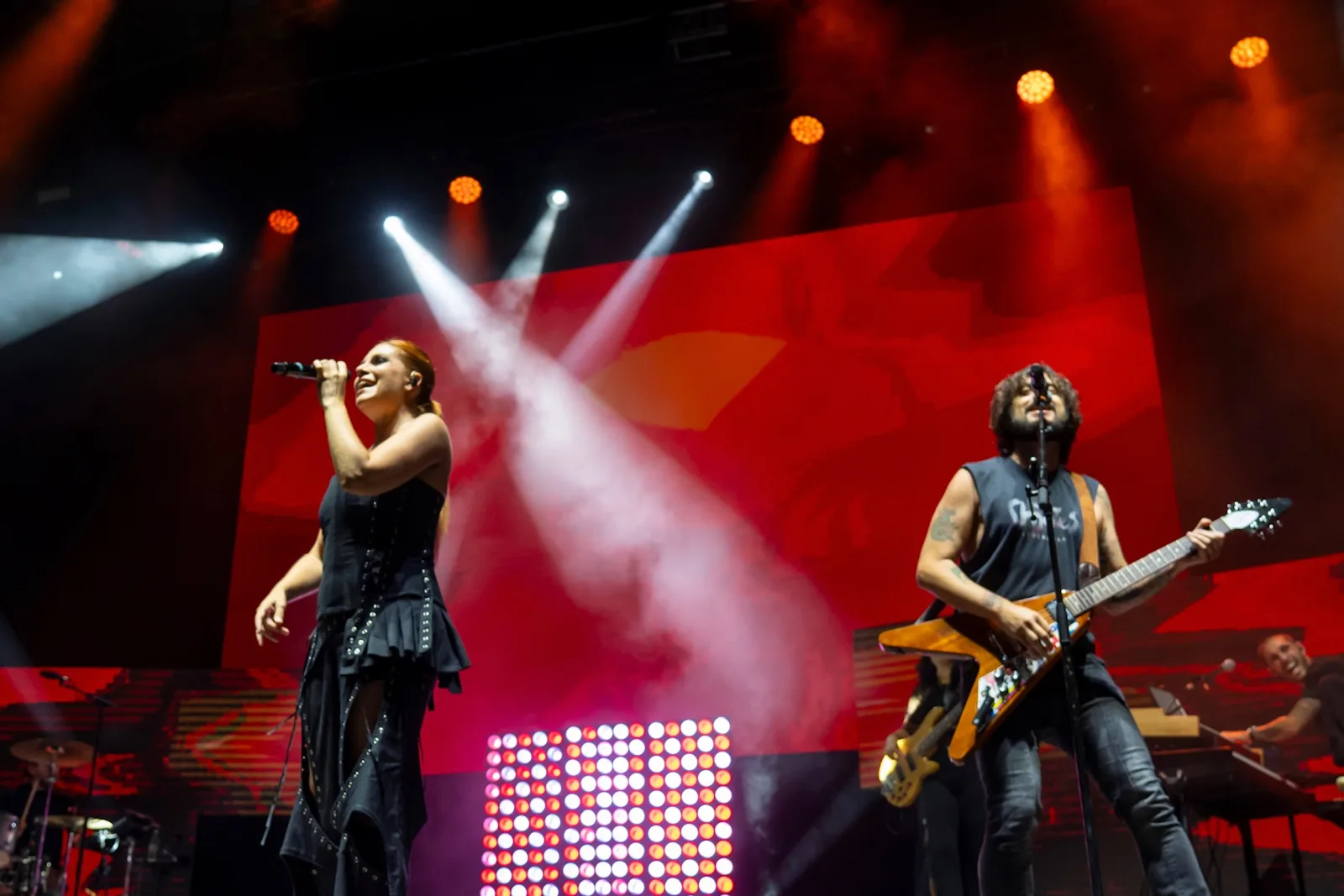 Leire Martínez canta junto al guitarrista, con la pantalla del escenario iluminada en rojo detrás