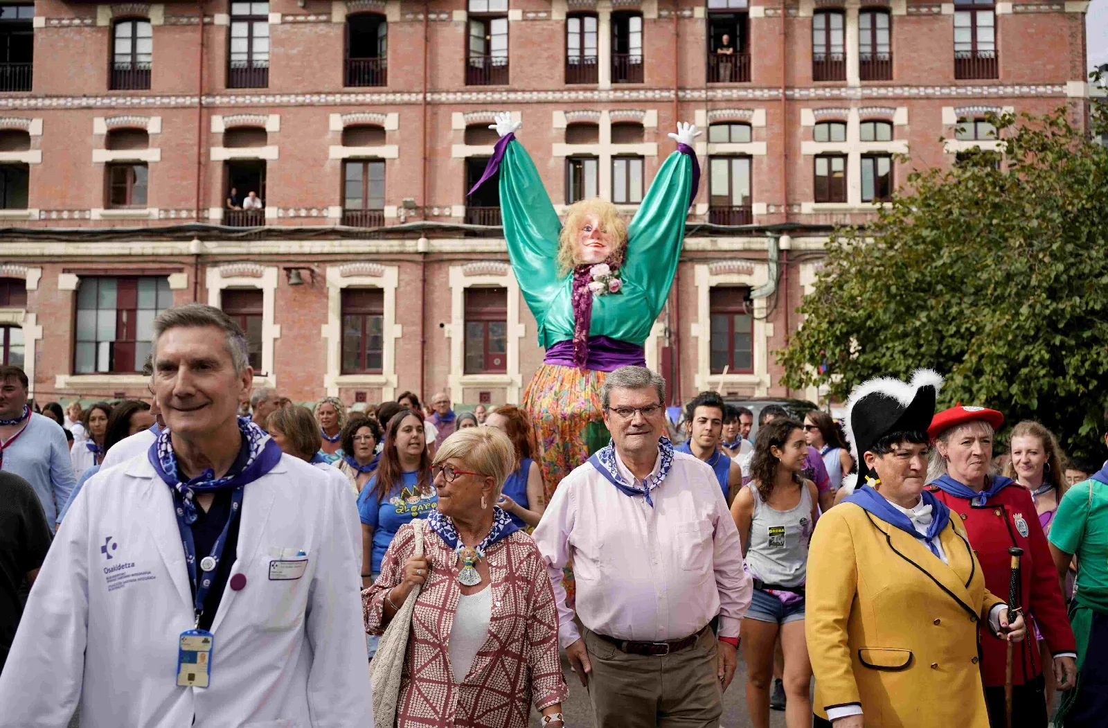 Marijaia con los brazos en alto entre la comitiva, delante de la fachada de ladrillo de un pabellón del Hospital de Basurto