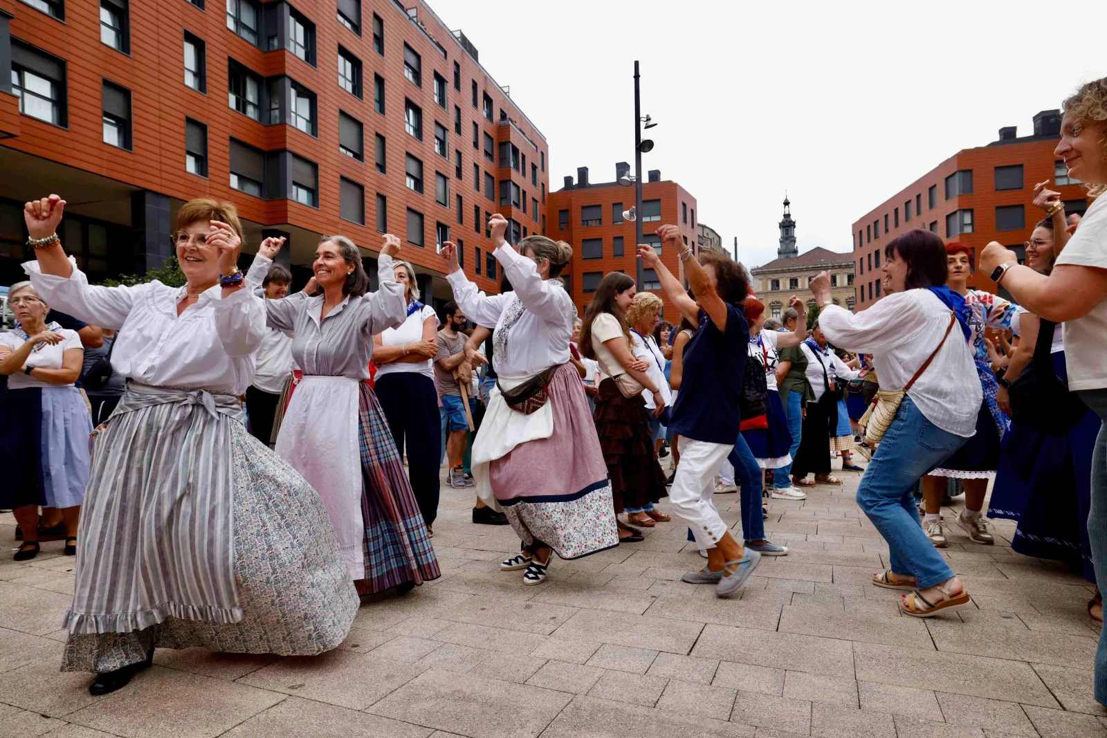 Un grupo de mujeres con falda y delantal tradicionales baila con los brazos en alto entre el resto del público