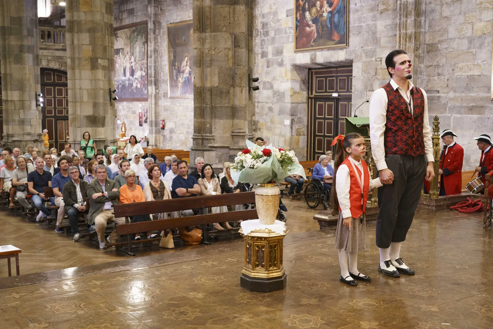 Artistas de circo durante la ofrenda floral en la basílica, ante el público sentado en los bancos