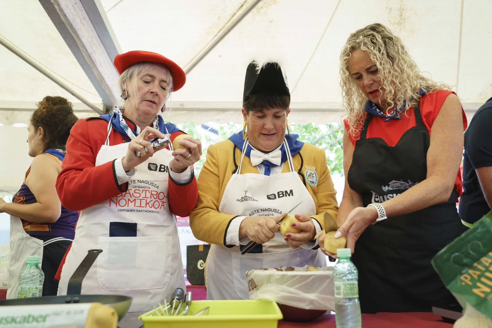 Tres participantes con indumentaria de fiestas pelan patatas sobre una mesa del certamen