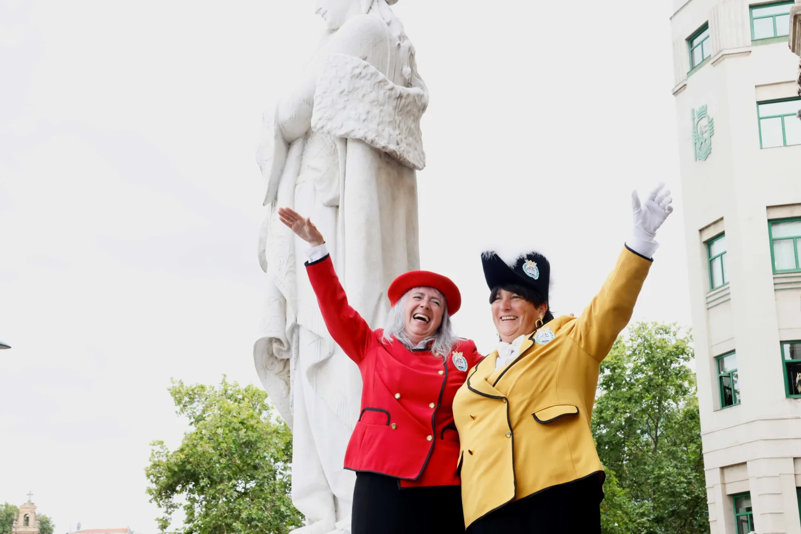 La pregonera y la txupinera saludan con los brazos en alto junto a una estatua