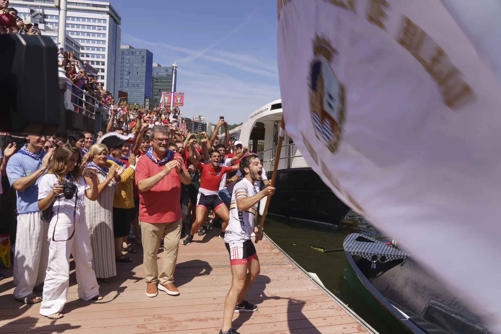 Un remero corre con la bandera por el pantalán ante el público