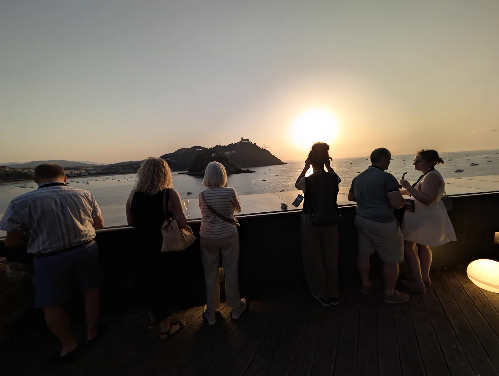 Un grupo de asistentes, de espaldas y en penumbra, asomados al muro de la terraza del Aquarium mirando al sol sobre la isla de Santa Clara durante el eclipse