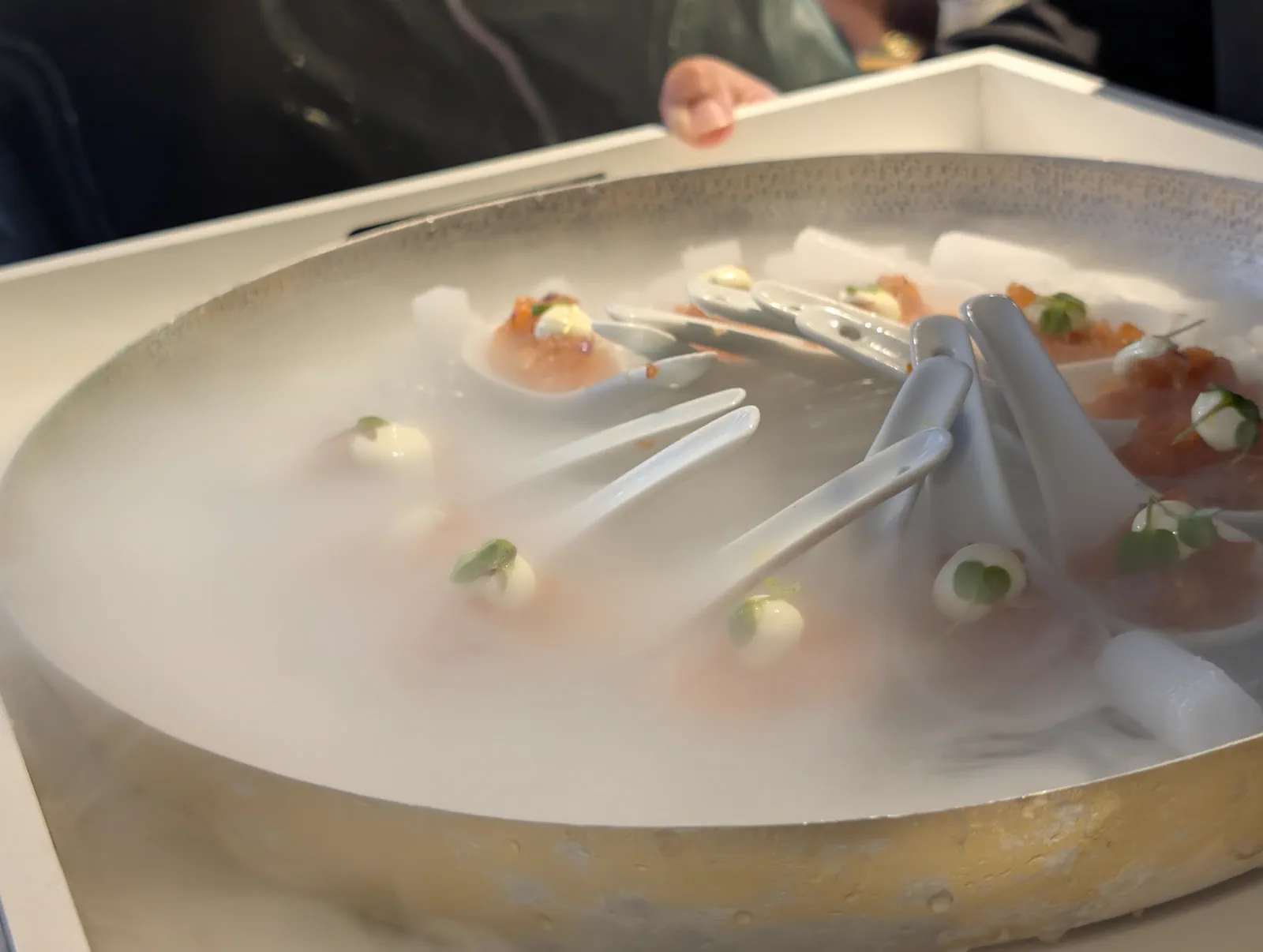 Bandeja redonda llena de hielo seco humeando con las cucharitas de salmón marinado con mahonesa al wasabi encima, en el momento de servirlas