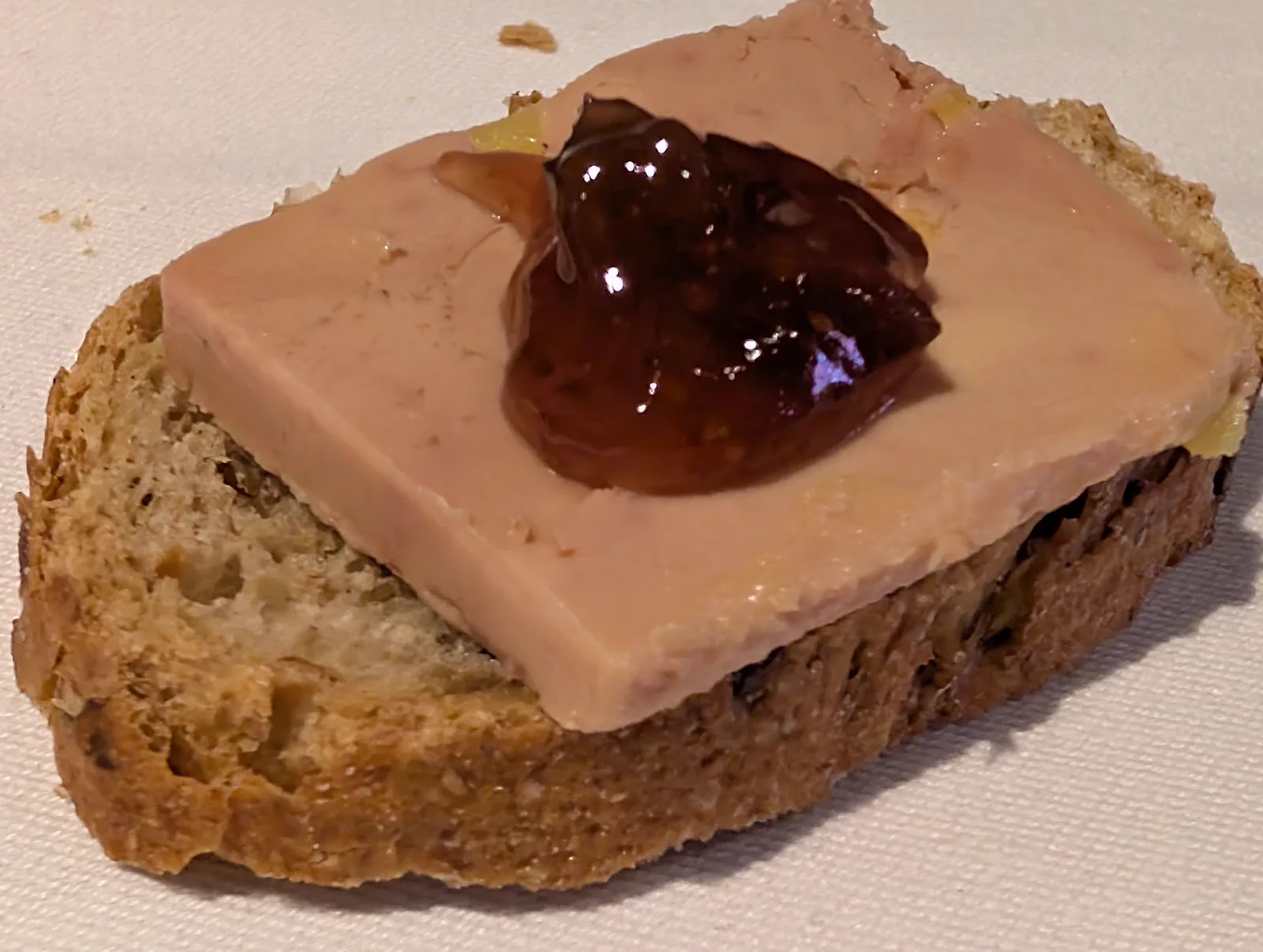 Rebanada de pan de cereales con una lámina gruesa de foie micuit y una cucharada de mermelada de higos encima