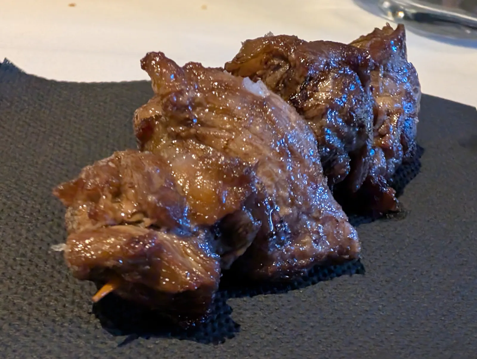 Brocheta de tres tacos de solomillo a la brasa glaseados, servida sobre una servilleta negra