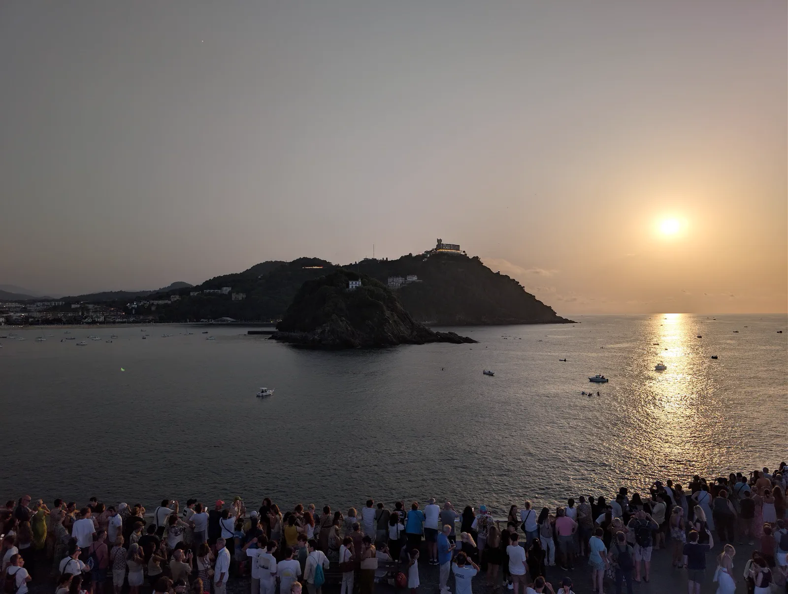 El Paseo Nuevo de Donostia completamente lleno de gente mirando al horizonte, con la isla de Santa Clara y el monte Igueldo al fondo, en el momento del máximo del eclipse