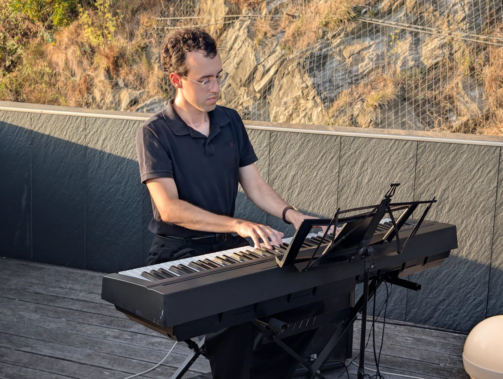 Un pianista tocando un teclado eléctrico en la terraza del Aquarium, con la ladera rocosa del monte Urgull detrás
