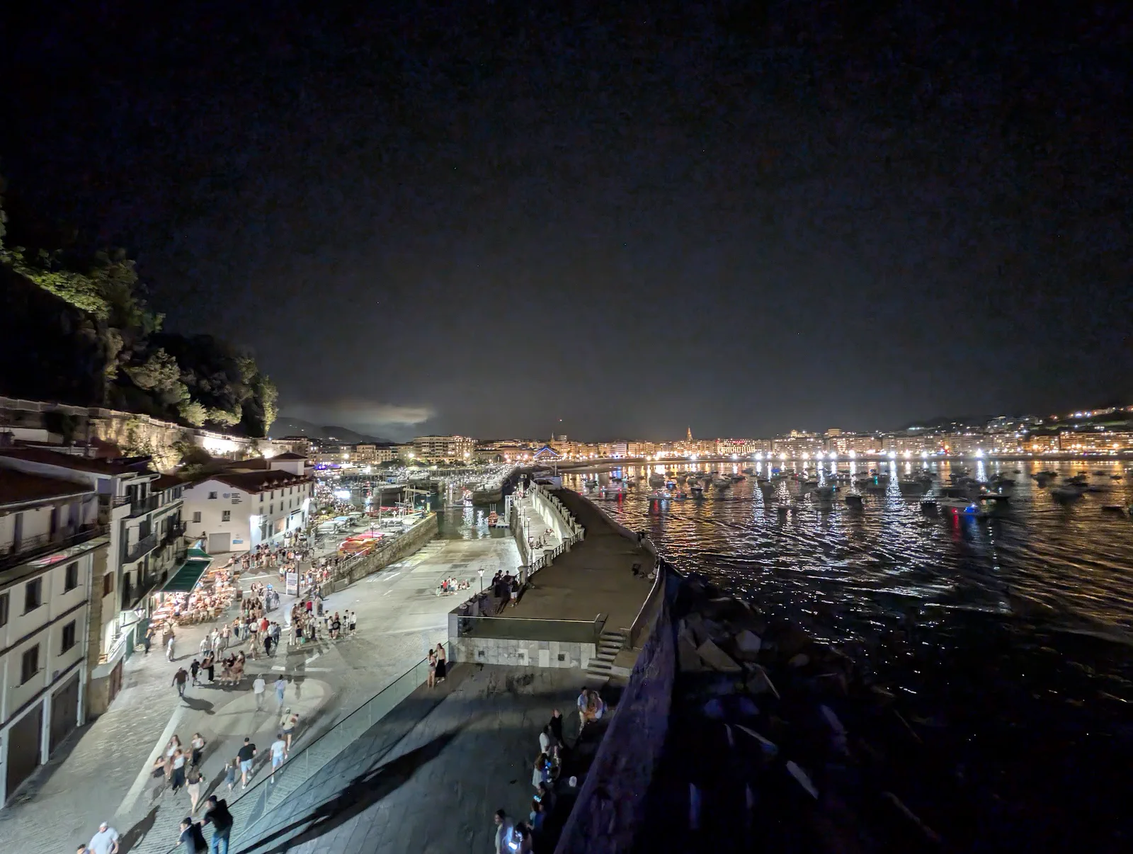 El puerto de Donostia y el Paseo Nuevo llenos de gente volviendo a casa después de los fuegos, con la bahía y la ciudad iluminadas al fondo