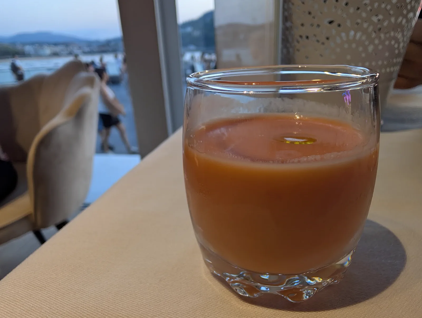 Vaso de salmorejo con un hilo de aceite de oliva sobre la mesa del Aquarium, con la bahía al otro lado del ventanal