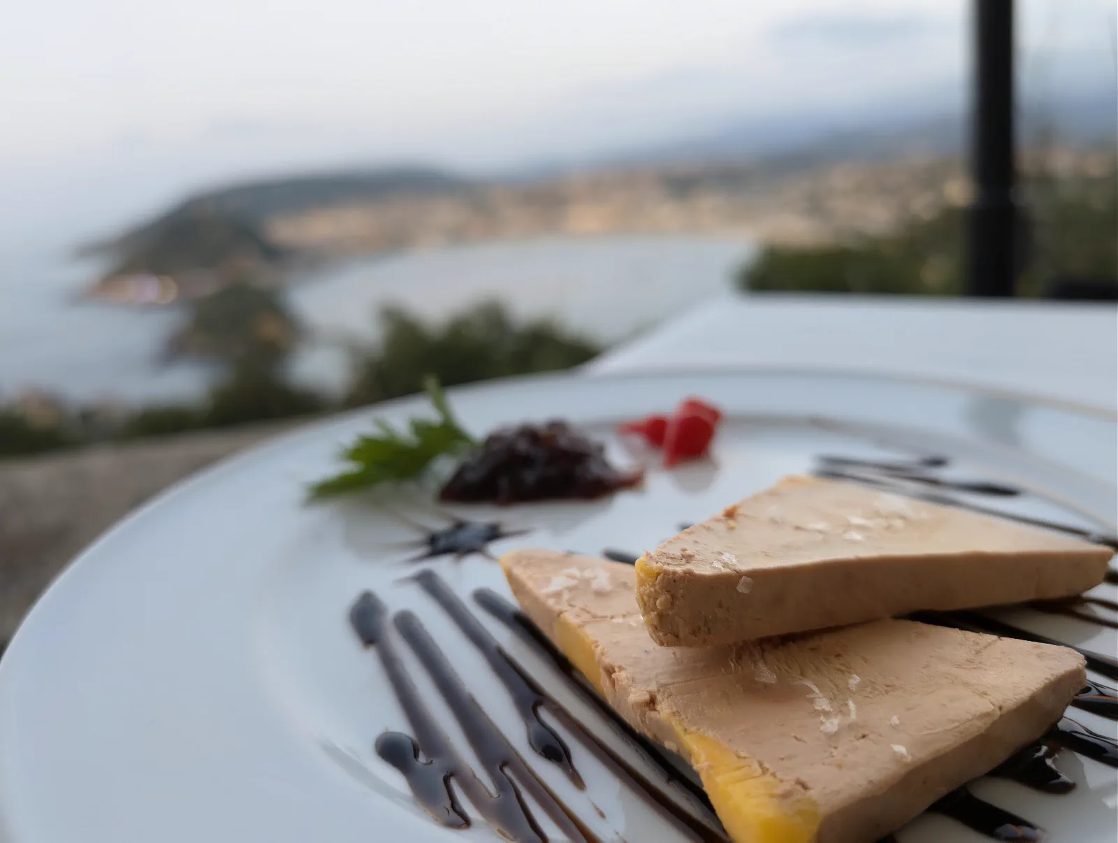 Dos láminas de foie micuit con cebolla caramelizada y reducción de Módena servidas en el Asador Alaia, con la bahía al fondo