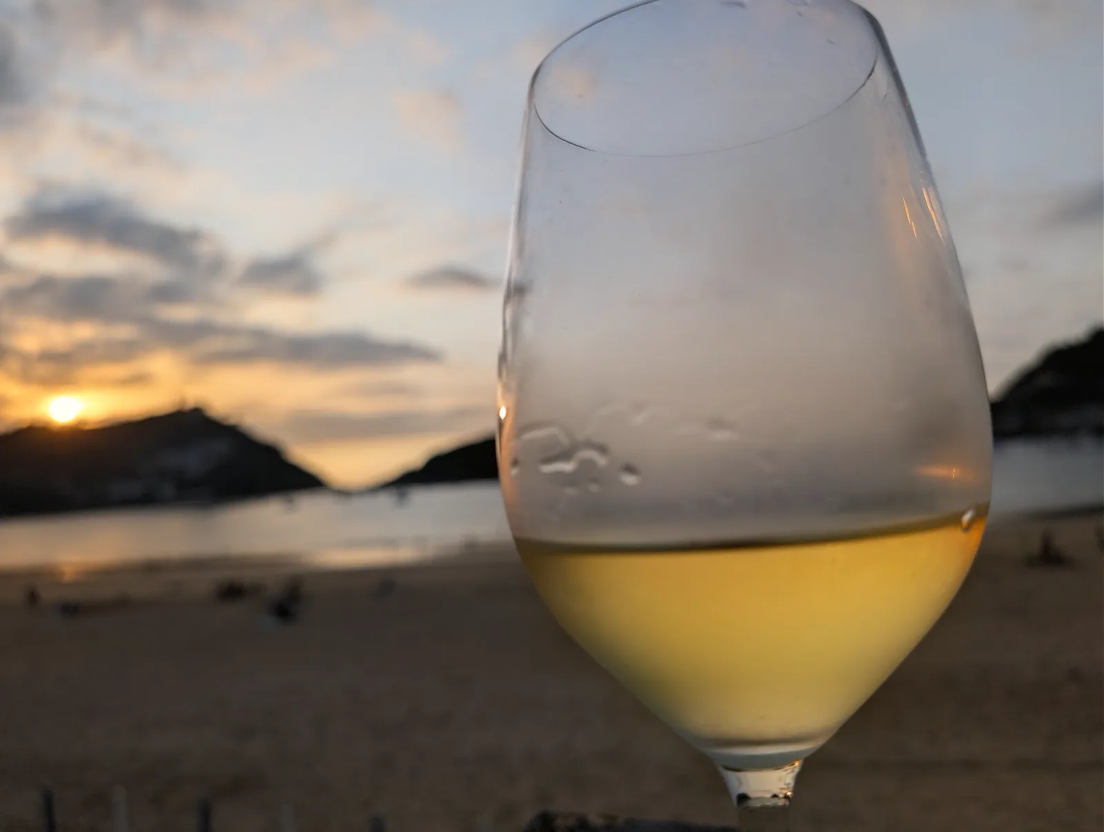Copa de vino blanco a contraluz con el sol poniéndose sobre el monte Igueldo y la playa de la Concha al fondo