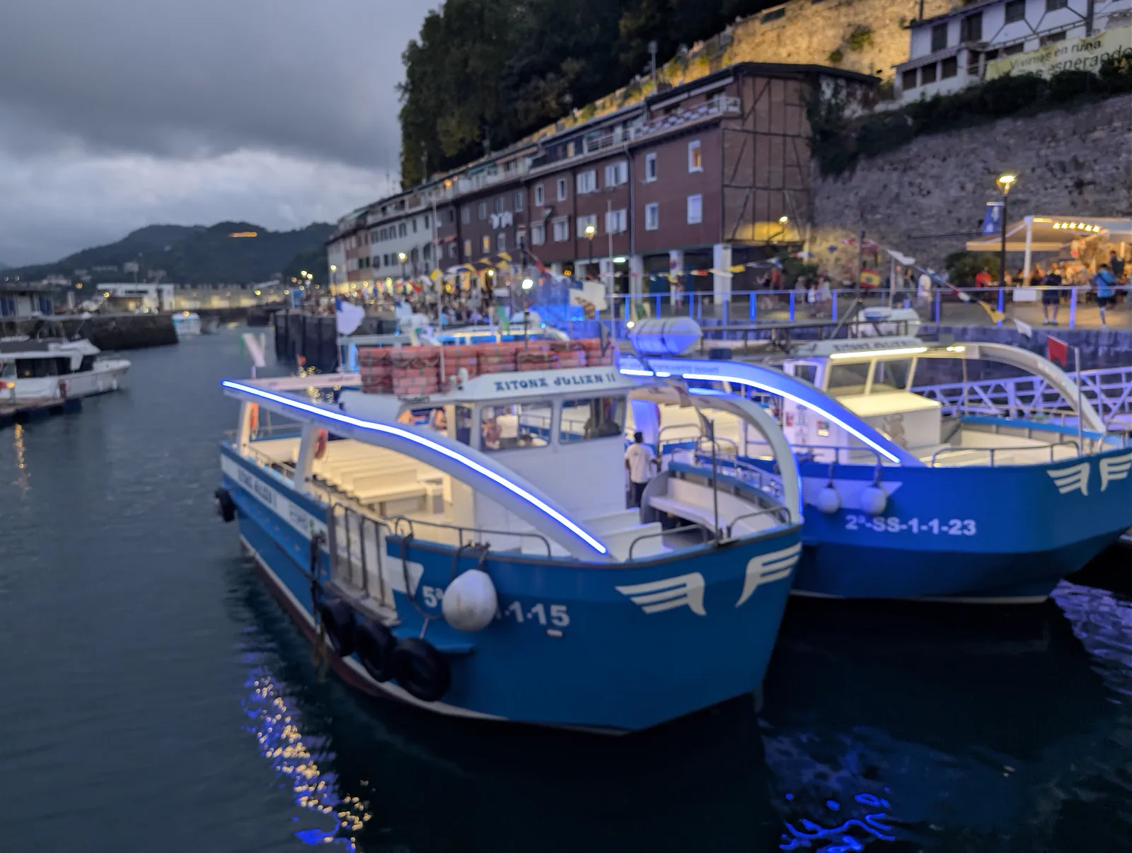 Dos motoras amarradas al anochecer con la tira de LED azul del arco ya encendida, reflejada en el agua del puerto
