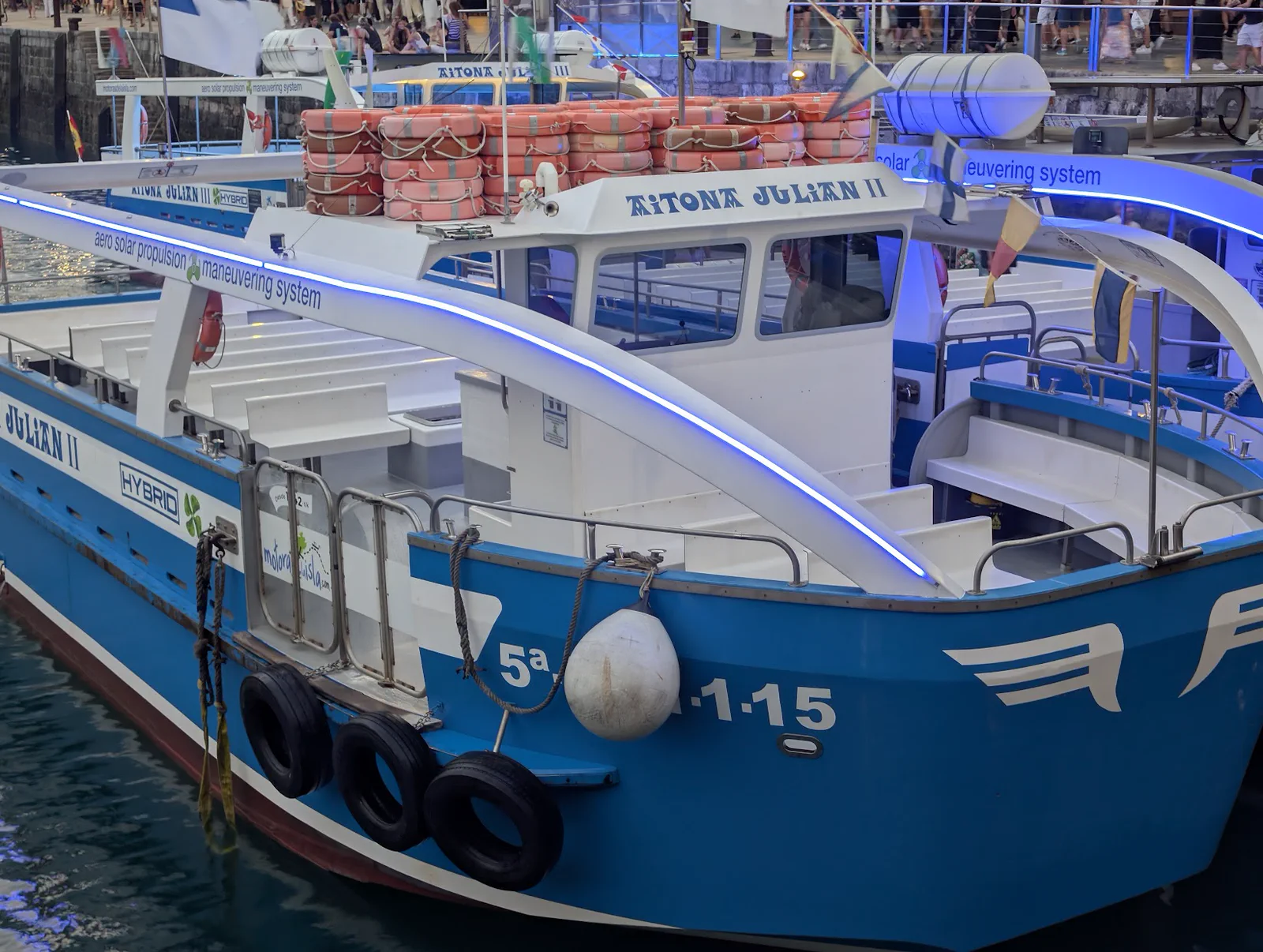 Proa del Aitona Julián II amarrada, con el rótulo HYBRID, los flotadores apilados en el techo y la tira de LED azul encendida recorriendo el arco