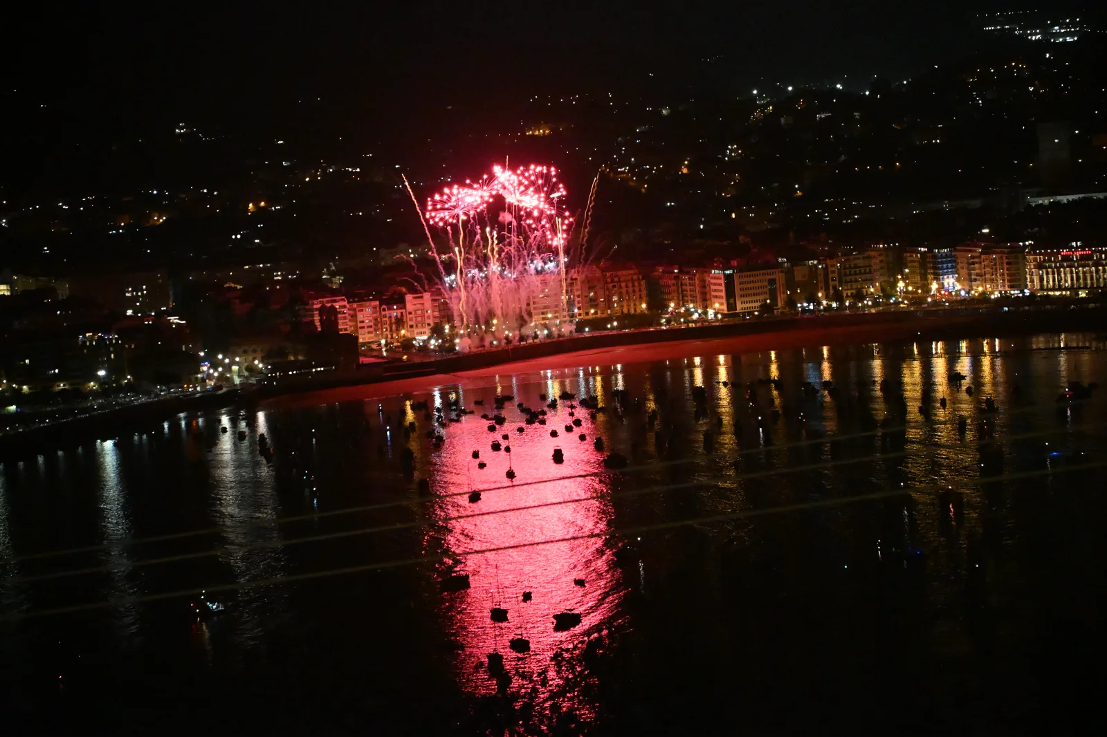 Ramillete de fuegos artificiales rojos sobre los edificios del paseo de la Concha, con la bahía teñida de rojo