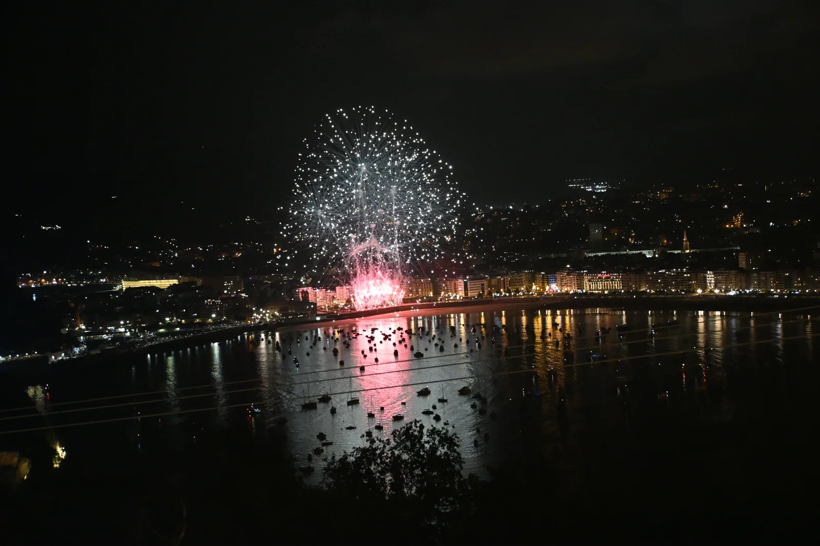 Estallido blanco y plateado de fuegos artificiales sobre Donostia con cascada de chispas cayendo hacia el paseo
