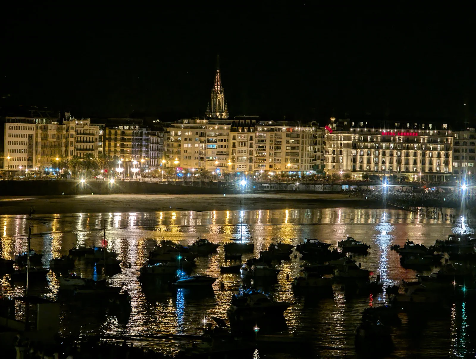 La bahía de la Concha de noche desde la terraza del Aquarium, con el paseo iluminado, la playa vacía y decenas de barcos fondeados esperando el primer disparo
