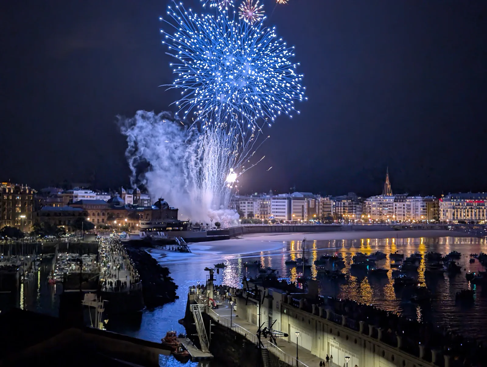 Gran estallido azul de Pirotecnia Valenciana sobre el centro de Donostia visto desde el Aquarium, con el puerto, el Paseo Nuevo y la playa de la Concha en el encuadre