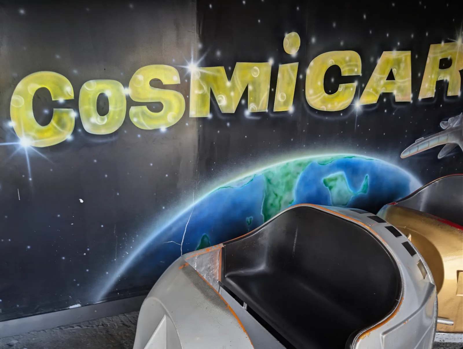 Mural espacial de la atracción Cosmicar del parque del monte Igueldo, con la Tierra pintada al fondo y una vagoneta blanca en primer plano