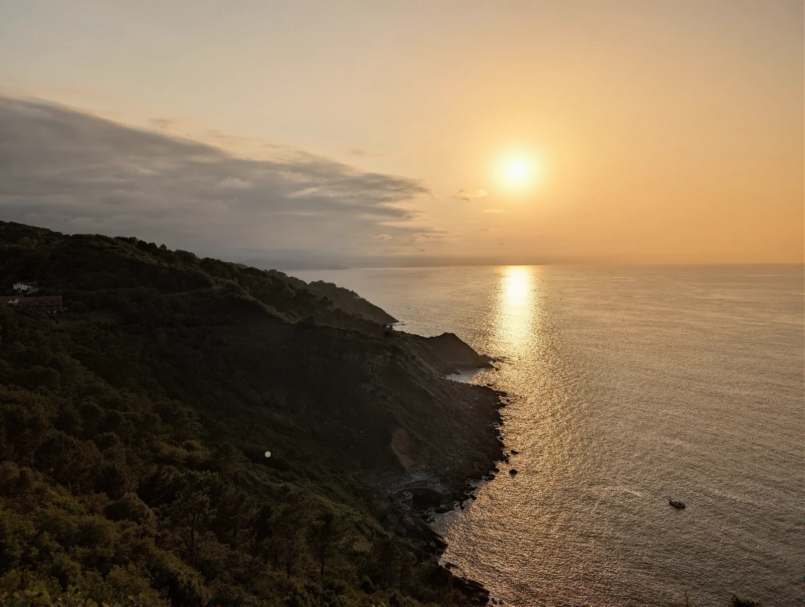 El sol poniéndose sobre el mar Cantábrico visto desde el monte Igueldo, con la costa en sombra en primer plano