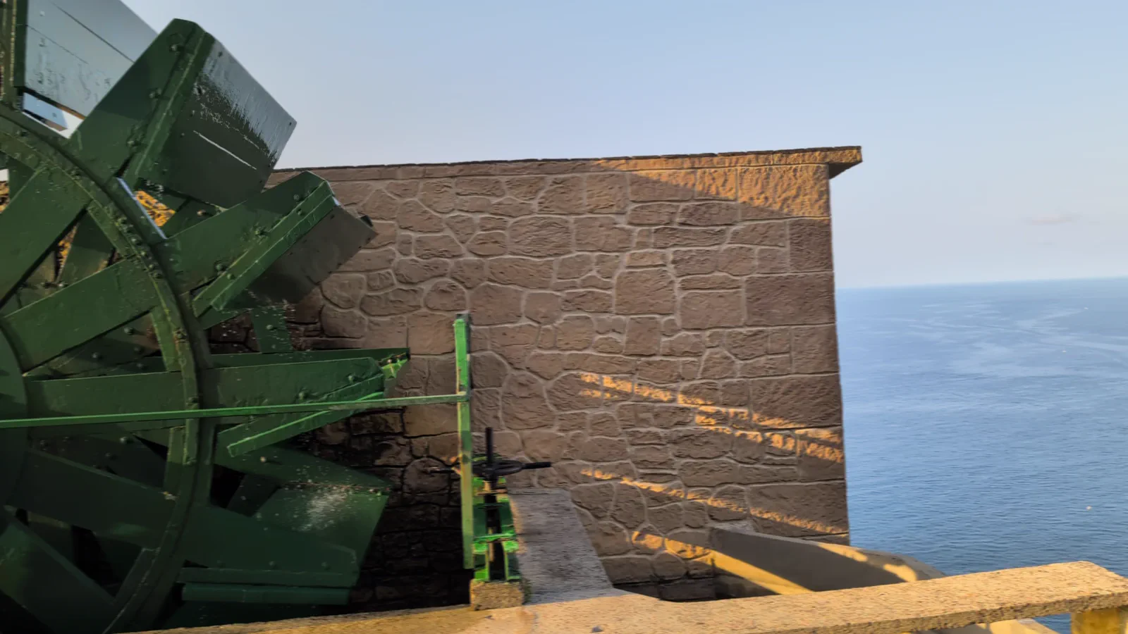 La gran rueda motriz de madera y hierro pintada de verde que mueve el agua del Río Misterioso, con el mar Cantábrico al fondo
