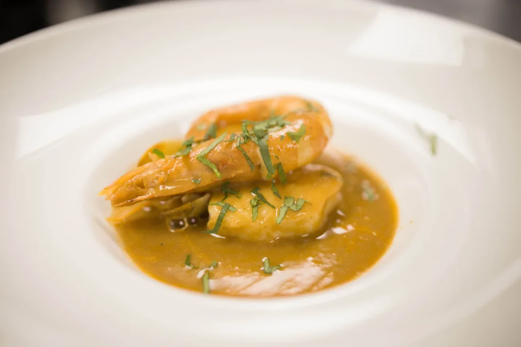 Langostinos en salsa marinera con perejil picado, emplatados en plato hondo blanco en Abakando