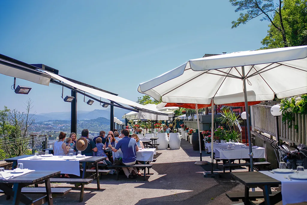 Terraza del Asador Alaia en el monte Igueldo con sombrillas y comensales frente a la bahía de la Concha