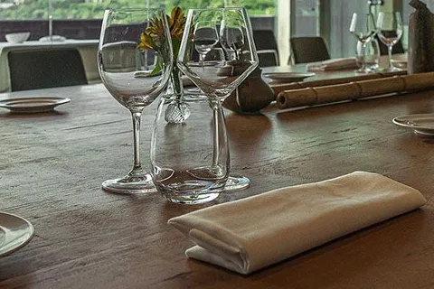Mesa de madera con copas y servilleta en el reservado de Bokado, con la ladera verde del monte a través del ventanal
