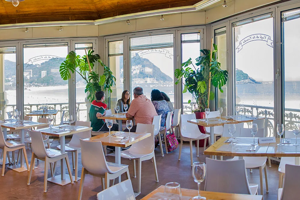 Comedor del Café de la Concha con grandes ventanales asomados al mar de la bahía