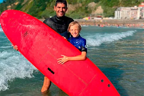Un monitor y un niño sujetan una tabla de surf de alquiler a la orilla de la playa de la Zurriola de Donostia