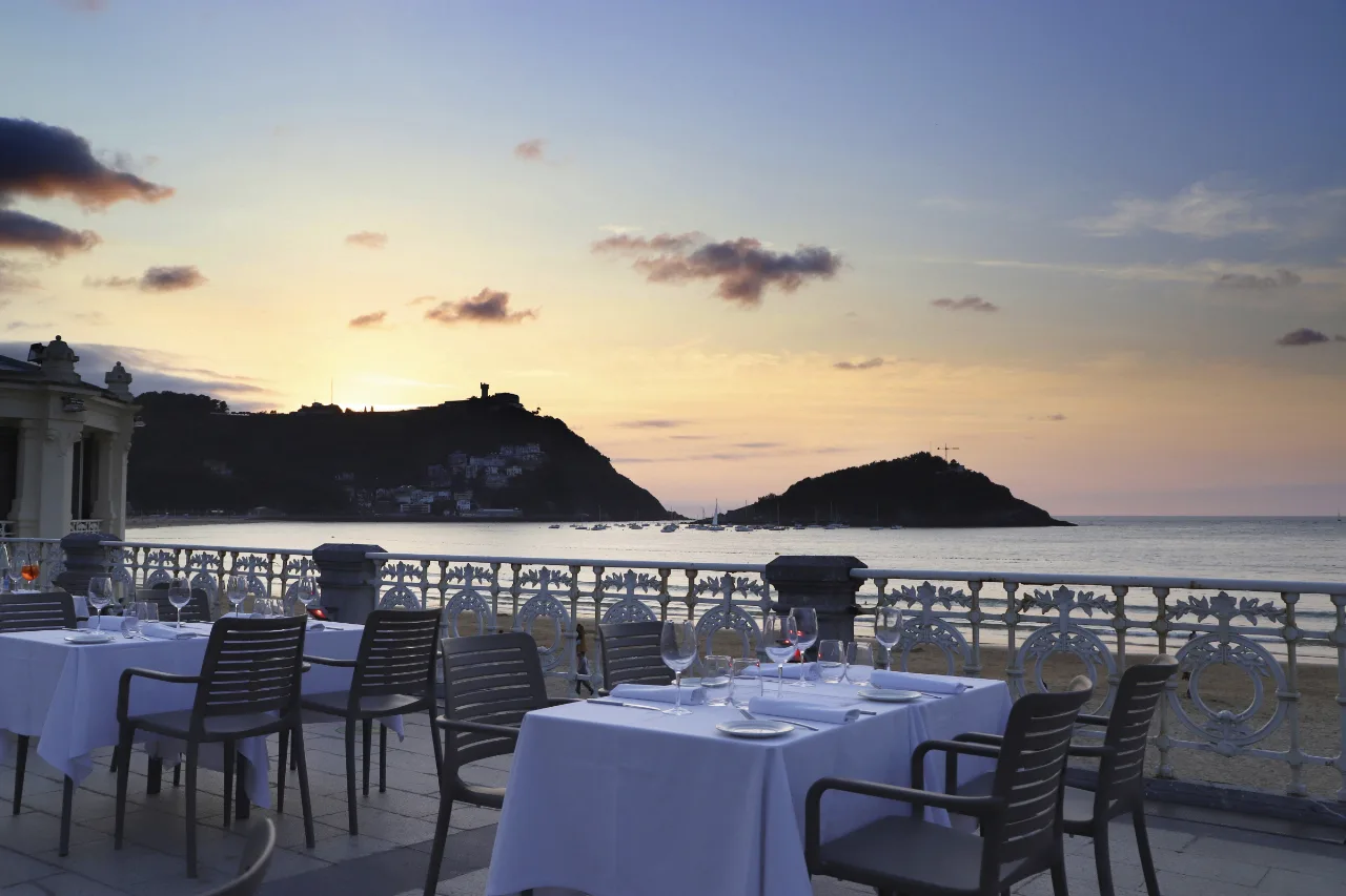 Terraza del Café de la Concha, en el edificio de La Perla, al atardecer, con mesas puestas frente a la bahía de la Concha