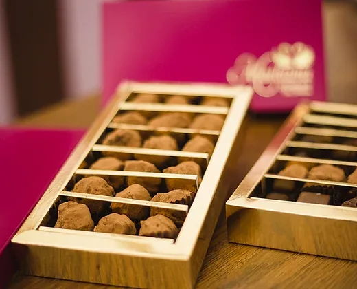 Bandejas doradas de trufas y bombones artesanos junto a un estuche de la Bombonería Maitiana