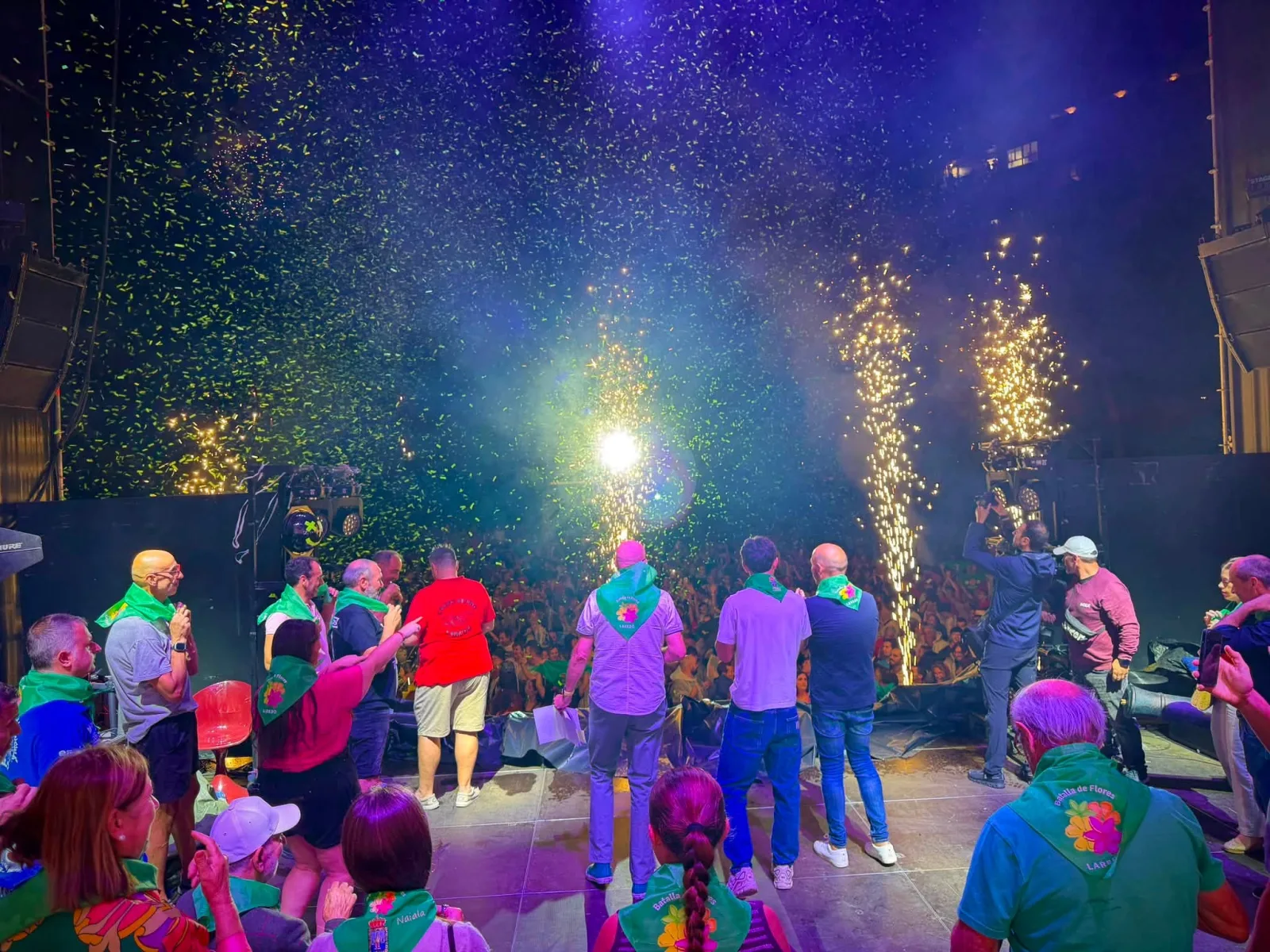 Carrocistas y autoridades con el pañuelo verde de la Batalla de Flores, sobre el escenario de la Alameda Miramar durante el chupinazo, entre confeti y chispas.