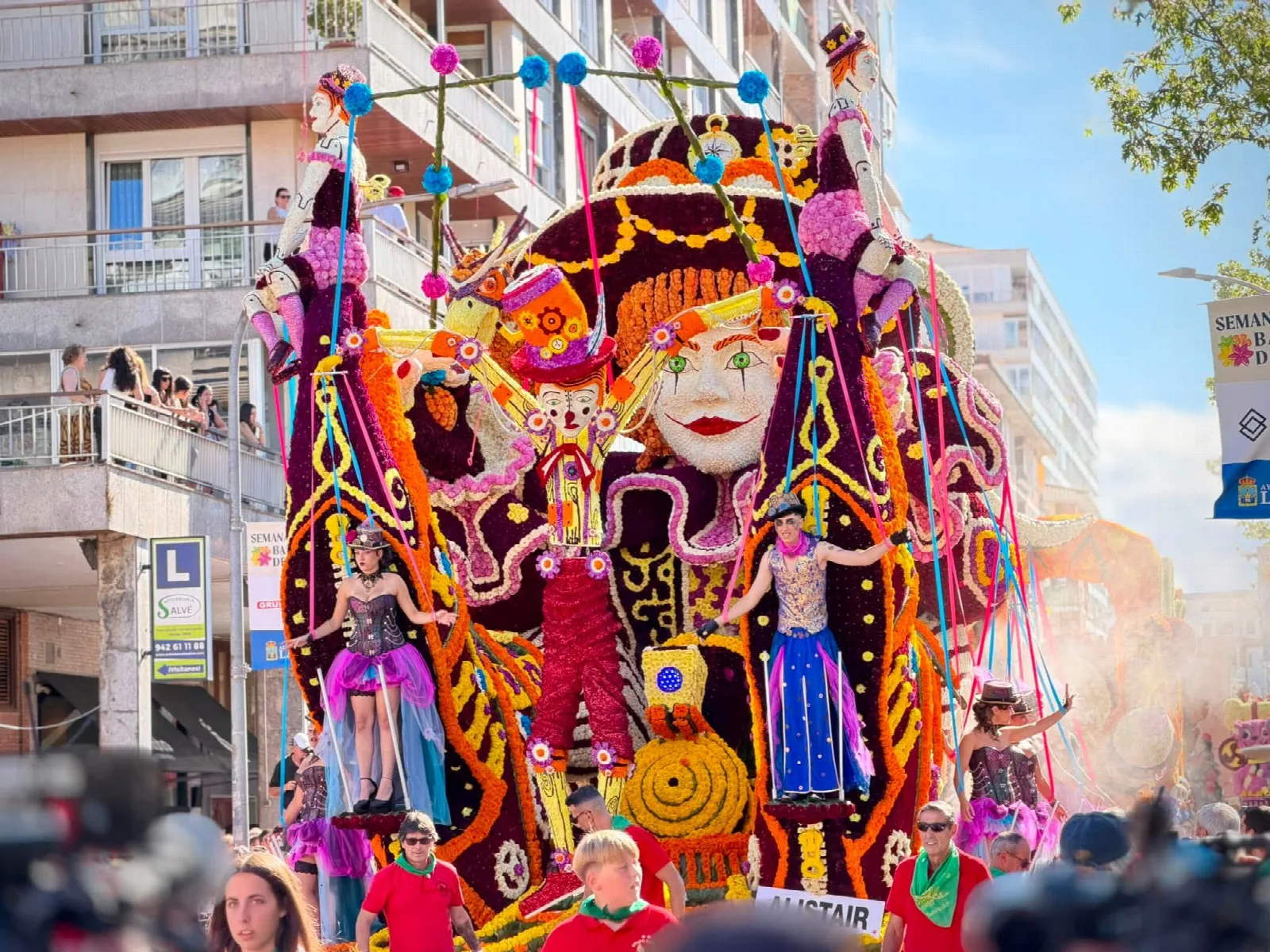Carroza de flor con una figura de niño de época y una marioneta articulada de gran tamaño, con la placa del título delante y personas con vestuario victoriano sobre la plataforma