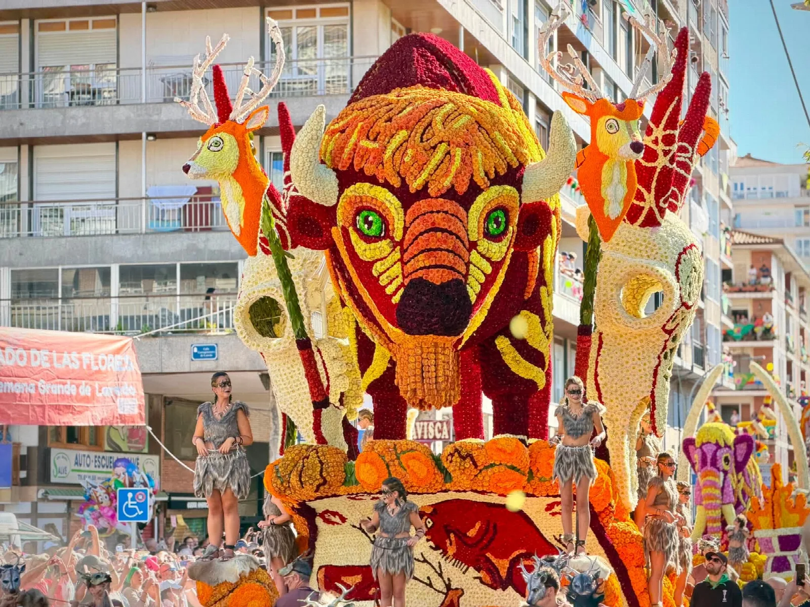 Carroza de flor natural con un bisonte monumental de las pinturas de Altamira flanqueado por dos ciervos, con varias personas vestidas con pieles sobre la plataforma