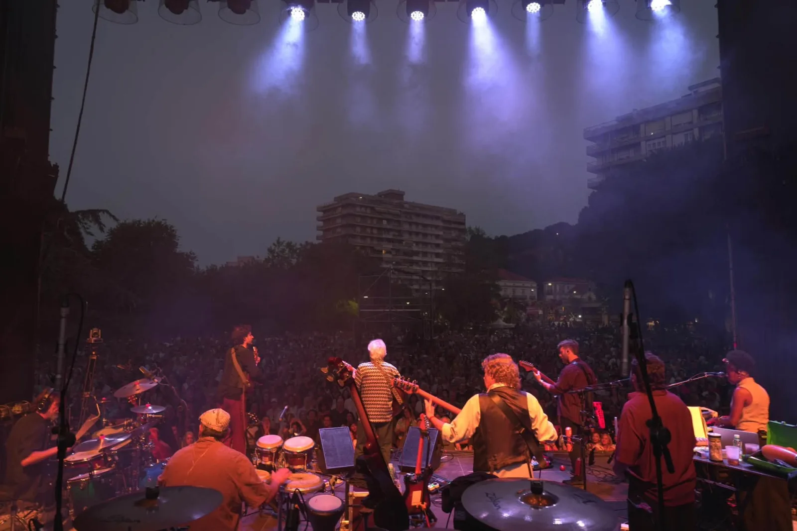 Vista nocturna desde el escenario con los focos encendidos sobre la banda en primer término y una gran masa de público extendiéndose hasta el fondo de la Alameda Miramar, con los edificios de Laredo iluminados detrás