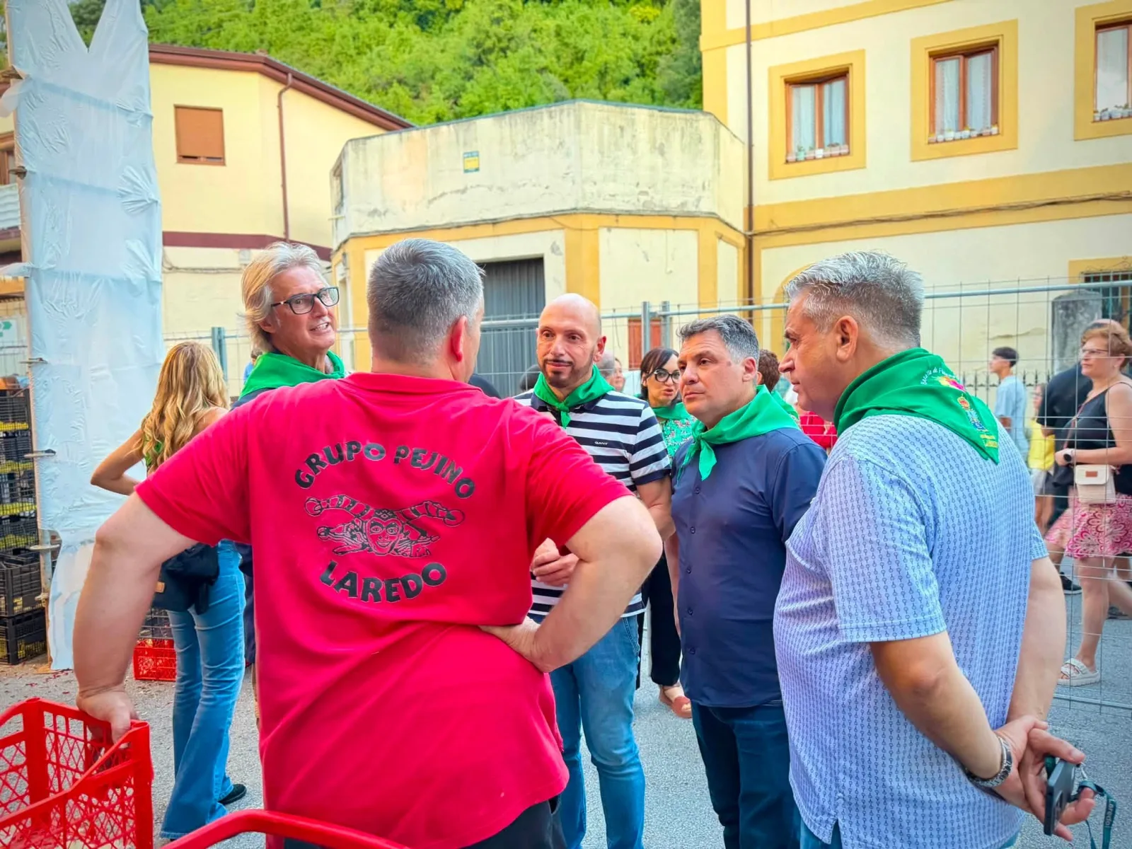 Varias personas con pañuelo verde de las fiestas conversando en la calle con un carrocista que viste una camiseta roja con el escudo del Grupo Pejino de Laredo