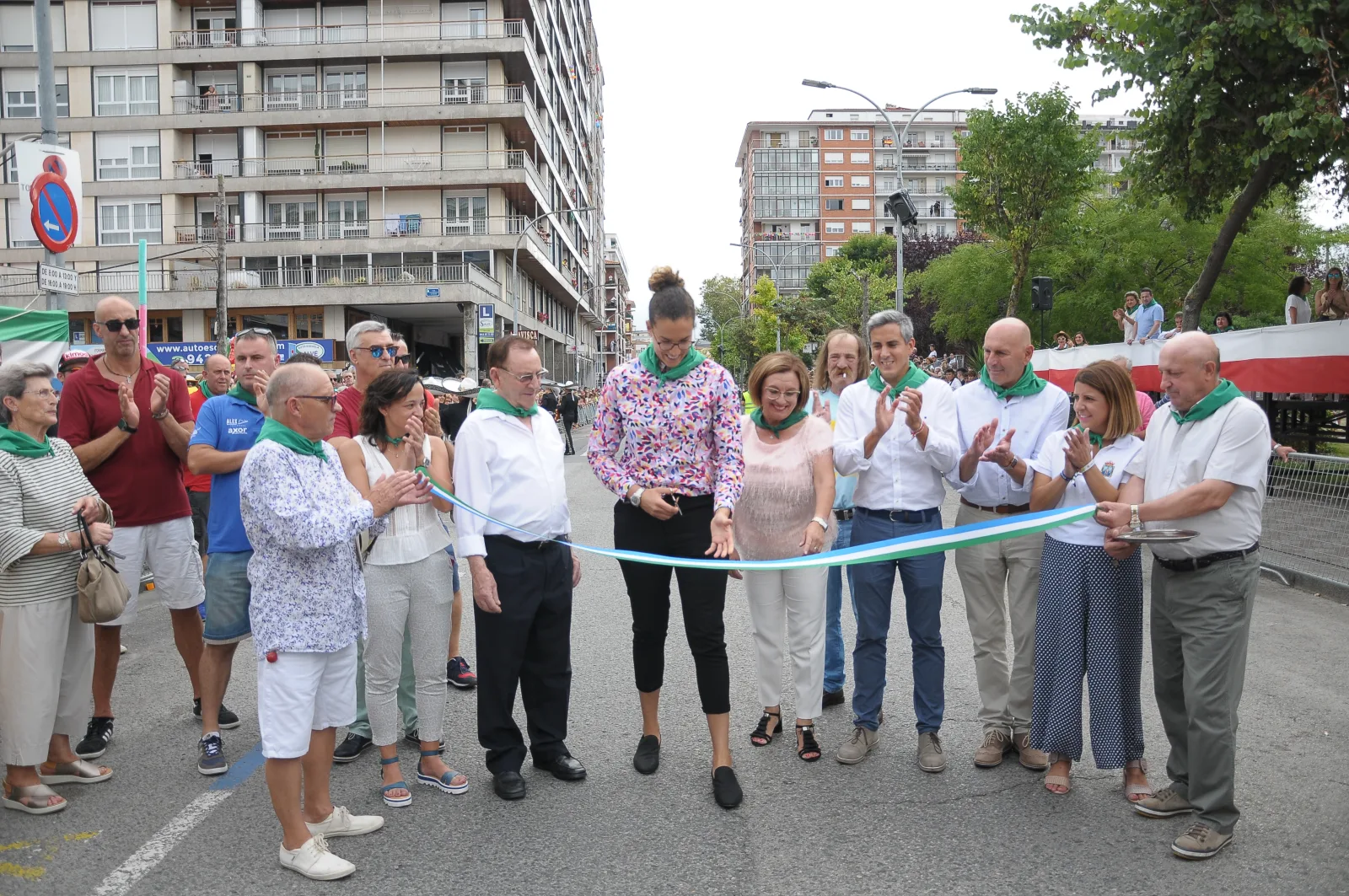 Corte de la cinta verde, blanca y azul que abre el circuito del desfile, rodeado de autoridades y vecinos con pañuelo verde.