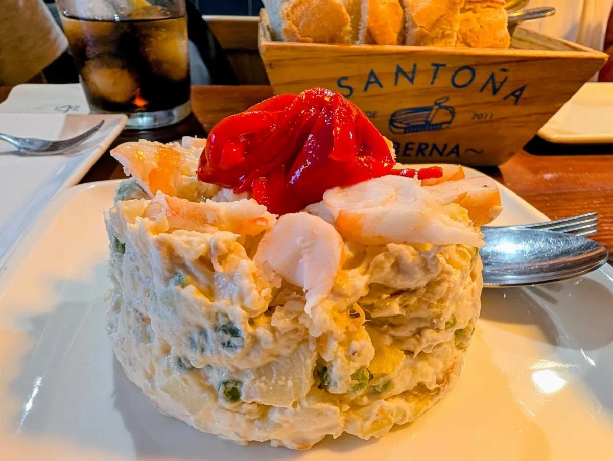Ensaladilla de la Taberna Santoña coronada con langostinos y pimiento del piquillo, junto a la caja de pan con el sello de la casa